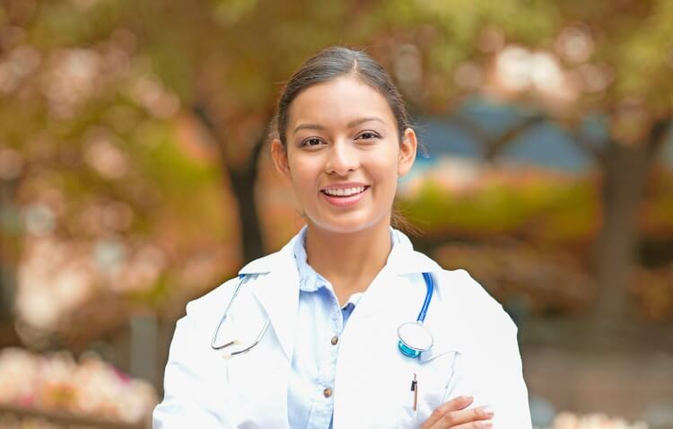 Nurse wearing a lab coat and smiling outside.
